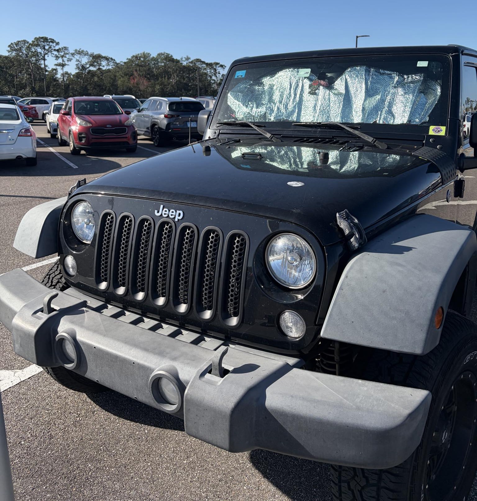 Black Jeep Wrangler with faded gray fender flares and bumper in a Florida parking lot